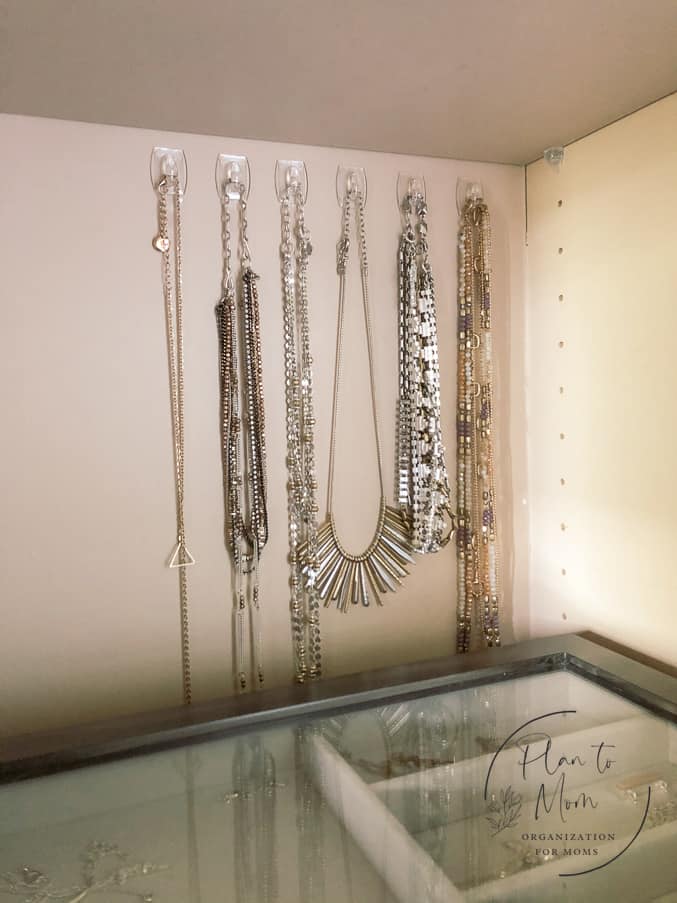 necklaces hanging on clear small command hooks on a shelf in a closet