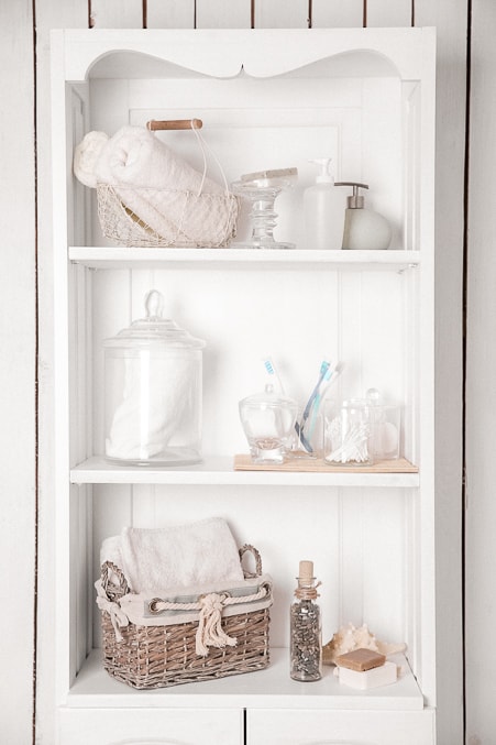 white wooden shelves mounted in the wall in a bathroom. three shelves containing various decor and bathroom items